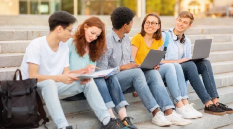 Étudiants discutant en groupe, avec ordinateurs et cahiers, illustrant l'apprentissage collaboratif et les formations à distance.